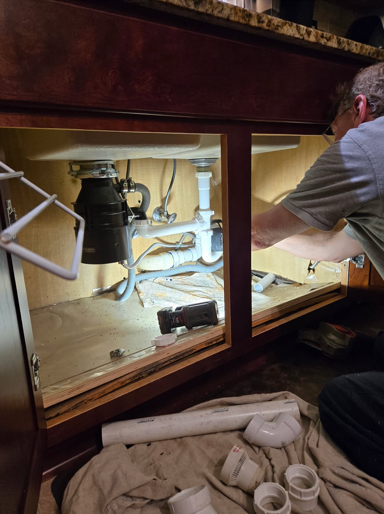A man is working under a sink in a kitchen.