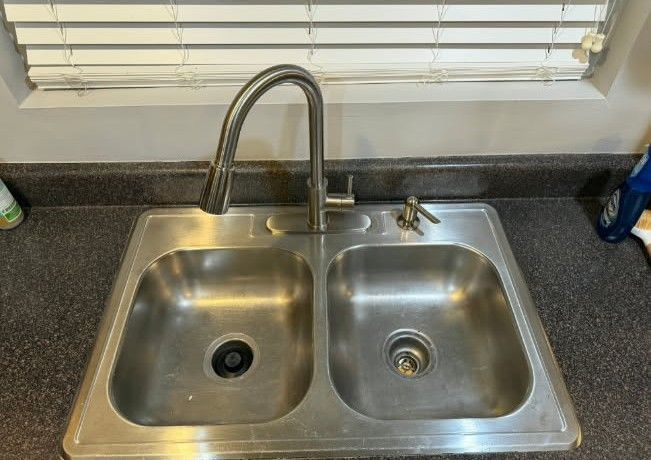 Stainless steel double kitchen sink with faucet, window, and soap.