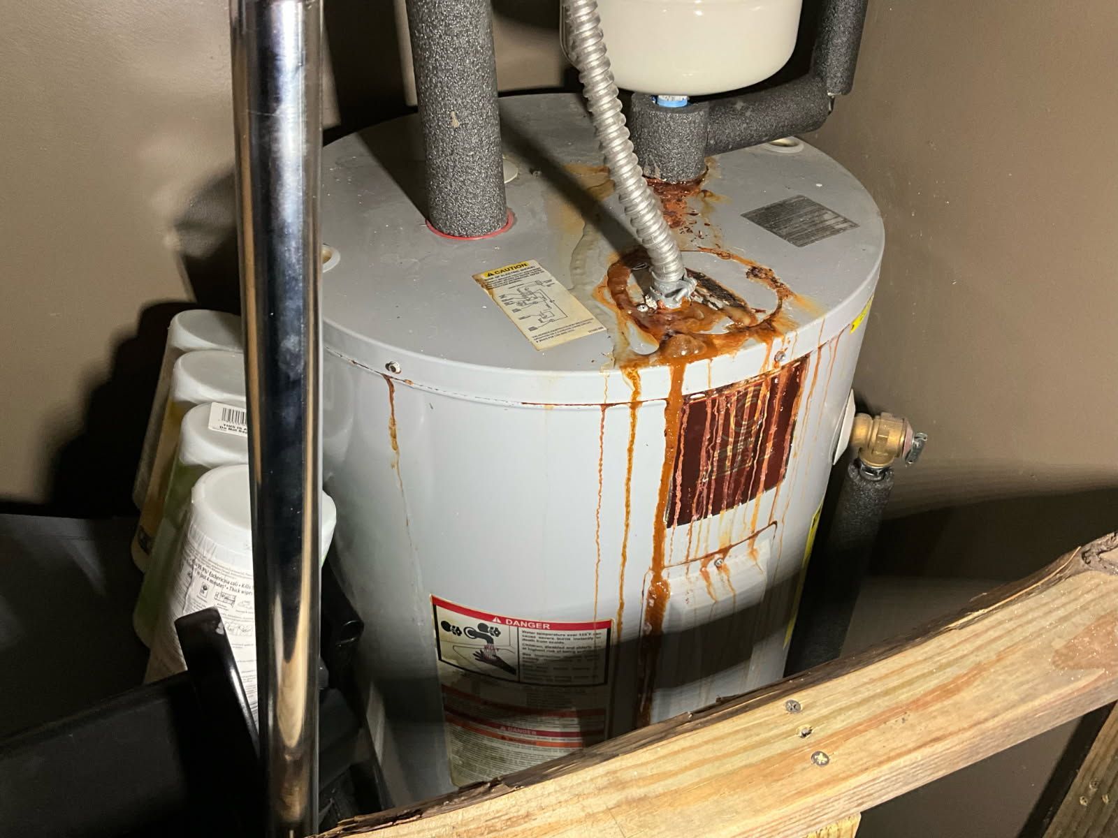 Leaking water heater, rust-colored streaks running down its side in an enclosed room.