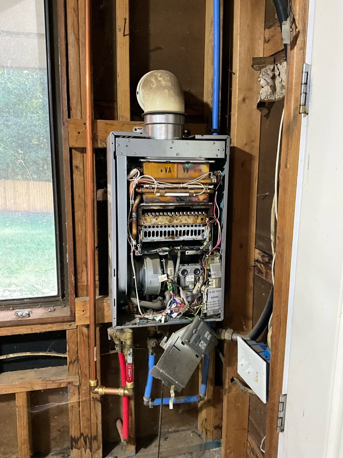 Tankless water heater installed in a wall; exposed internal components and plumbing.