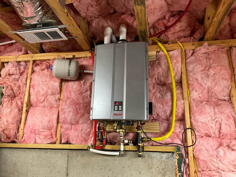 Tankless water heater installed on a wall, with pipes and insulation visible.