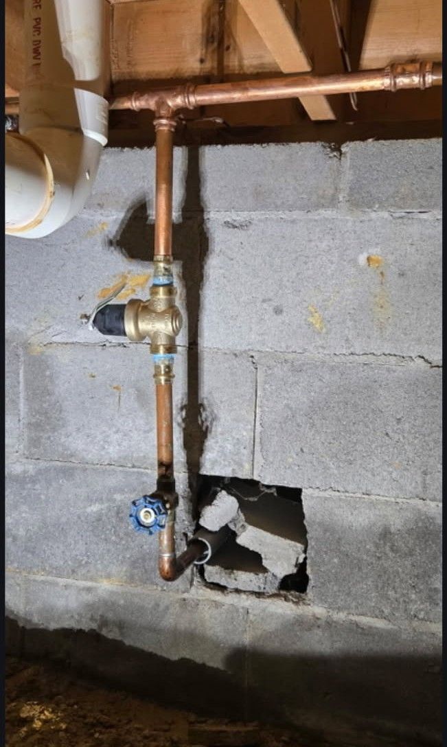 Copper pipes and valves attached to a concrete block wall, with a hole in the wall.