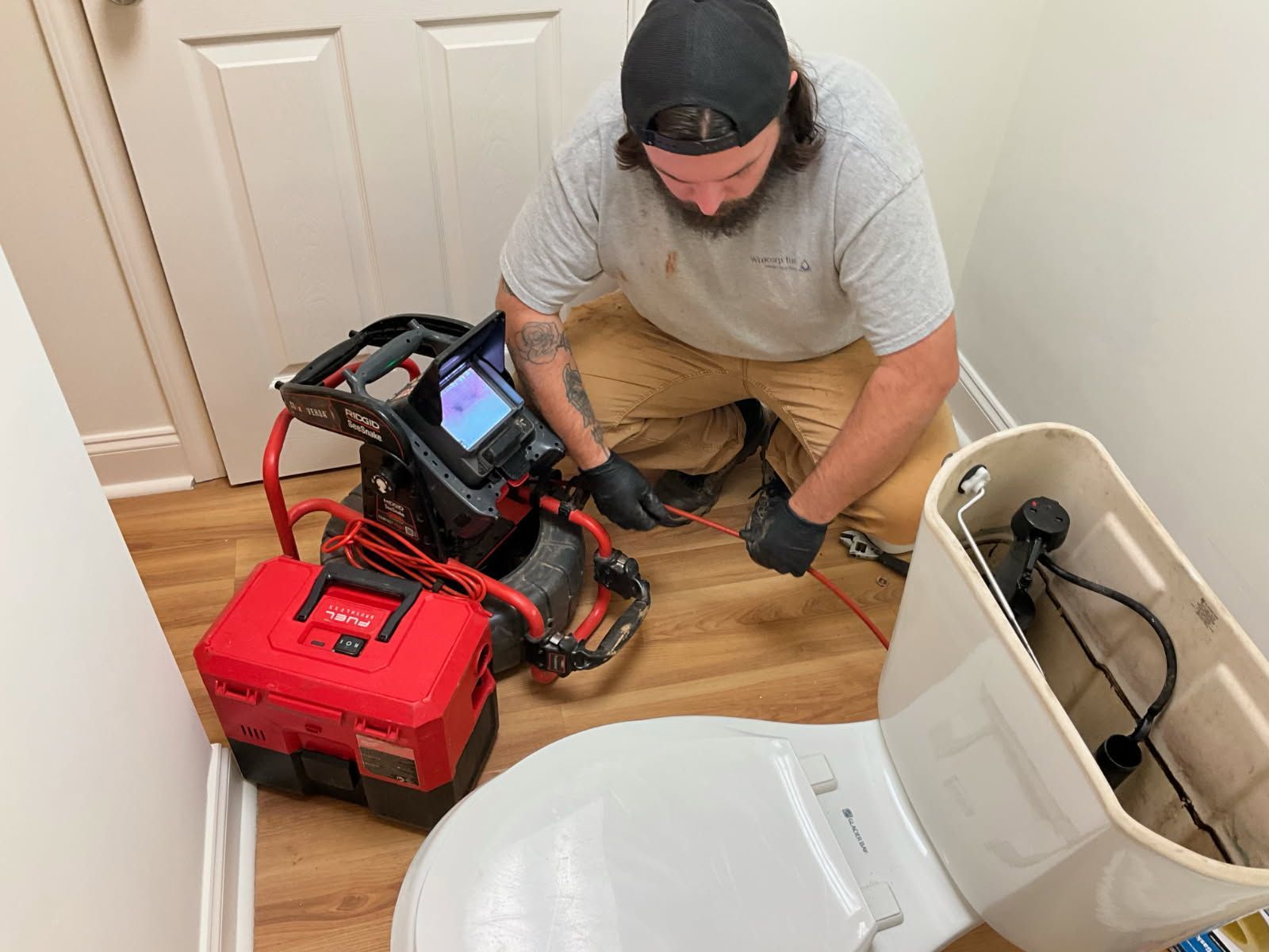 Plumber using inspection camera to examine toilet pipes in a small bathroom.