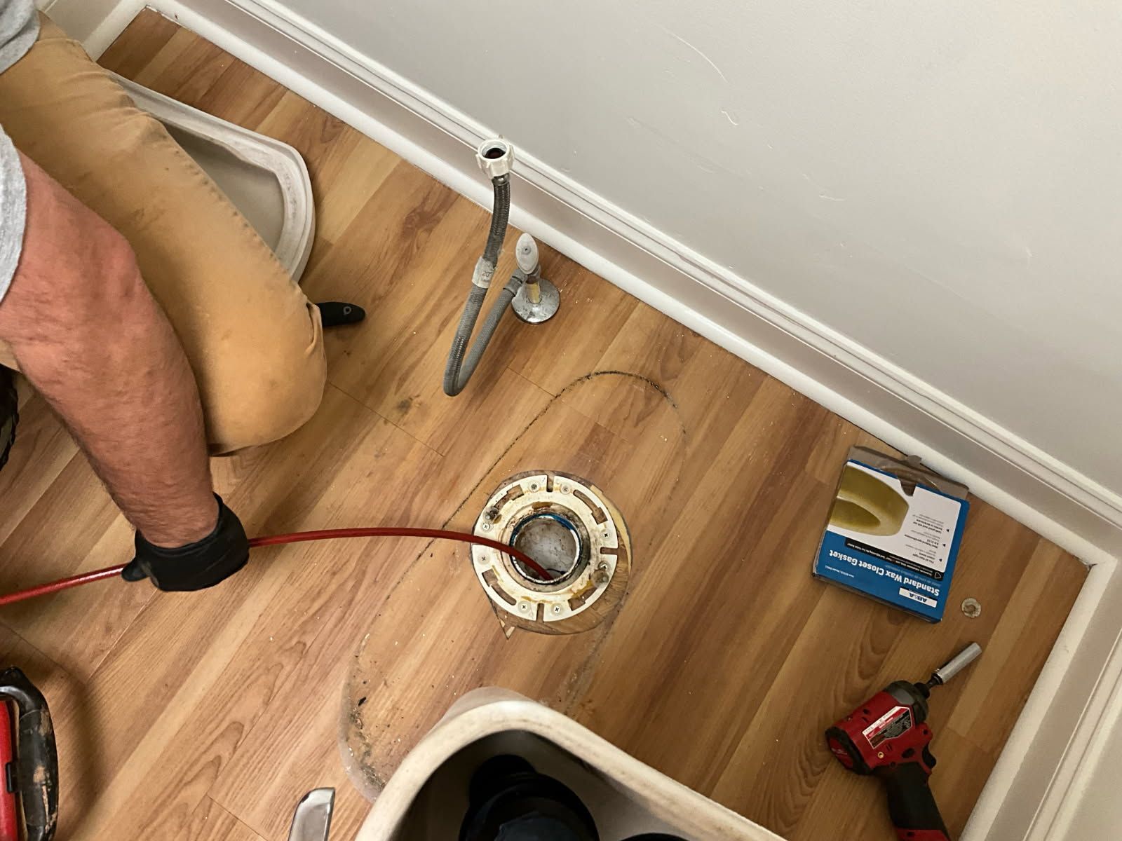 Person using a snake tool to clear a toilet drain, in a bathroom with new flooring.