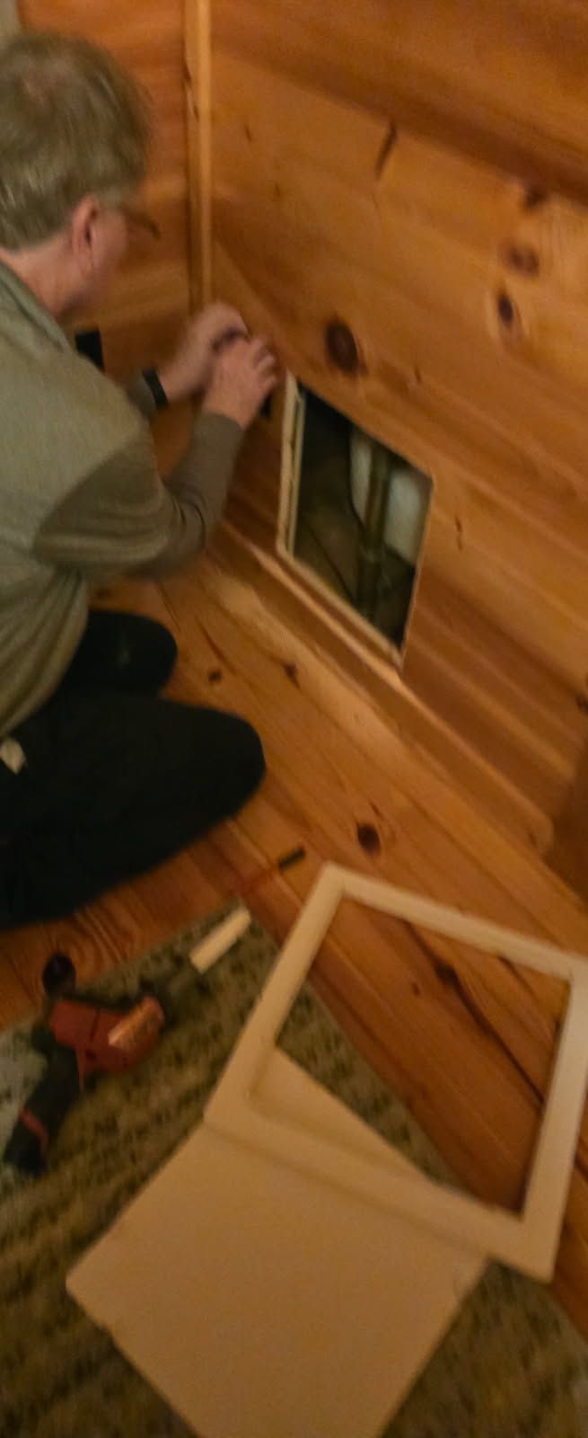 Person installing a vent cover on a wood wall inside a room.