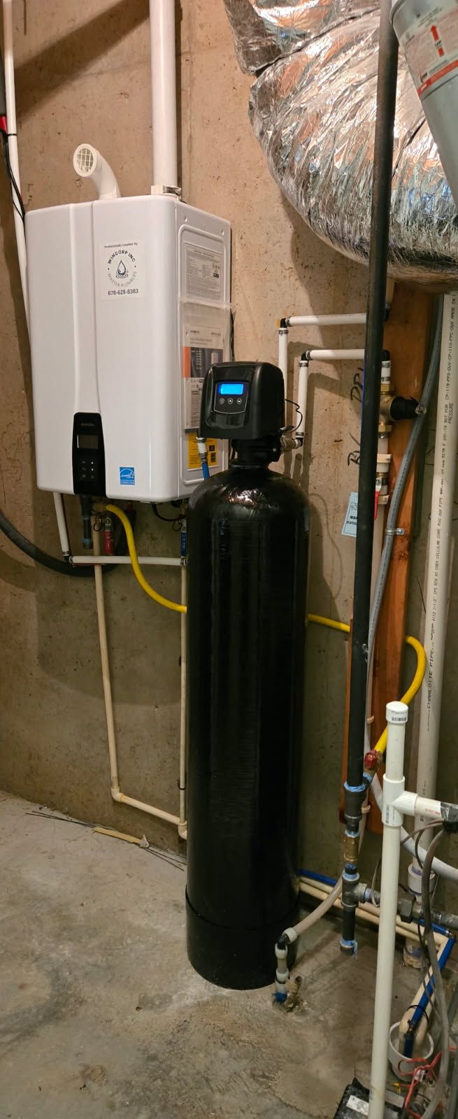 Water heater and water softener in a basement. White heater, black softener, pipes, and gray concrete floor.