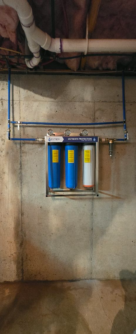 Water filter system installed on a concrete wall. Blue and white filters with supporting plumbing.