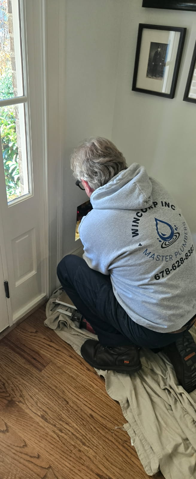 Person in a light blue hoodie crouches by a door, working on something, possibly installing or repairing.