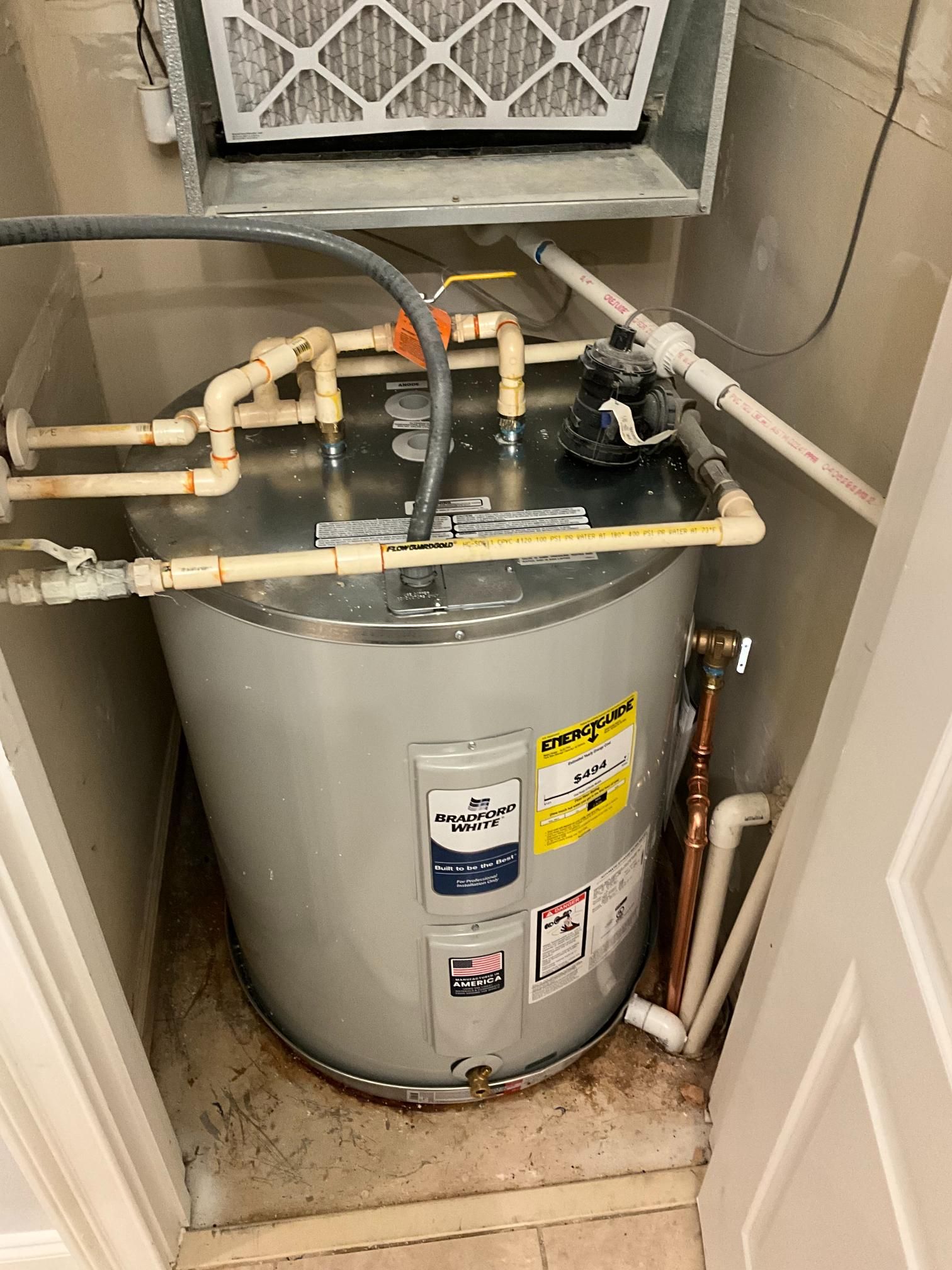 Water heater inside a small utility closet. Pipes, filter, and gas valve visible.