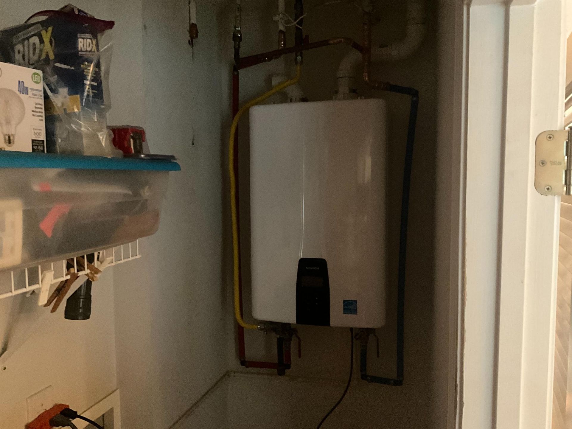 White tankless water heater in a utility closet with storage.