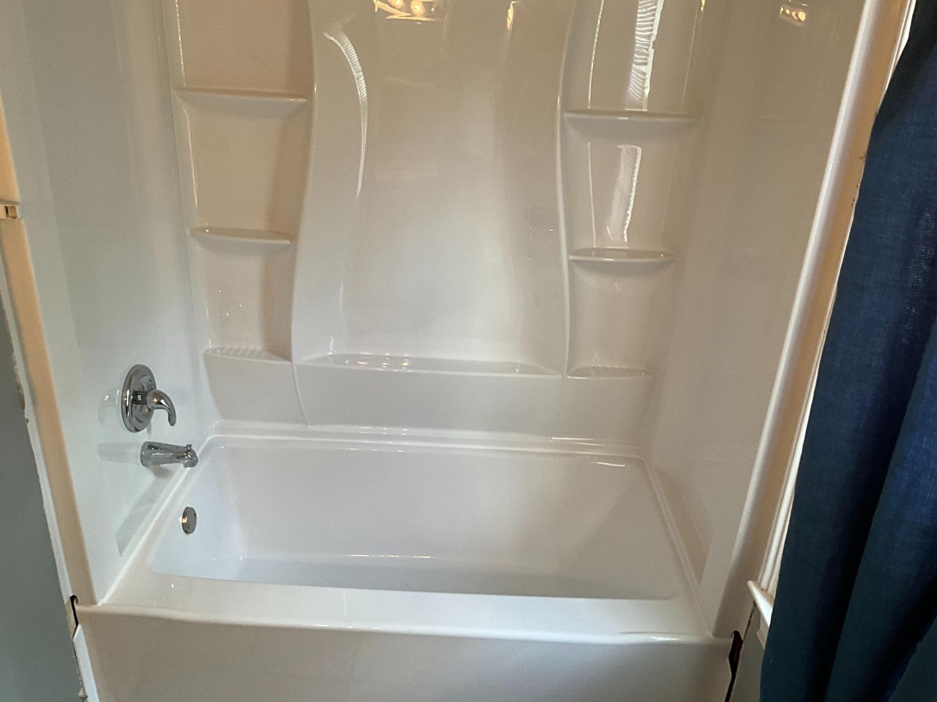 White bathtub and shower unit with built-in shelves and faucet.