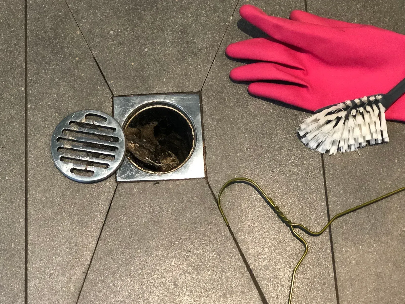 A person wearing pink gloves is cleaning a drain with a brush.