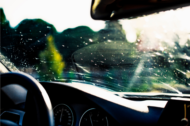 View from inside a car through a wet windshield, with blurred trees and bright sunlight ahead