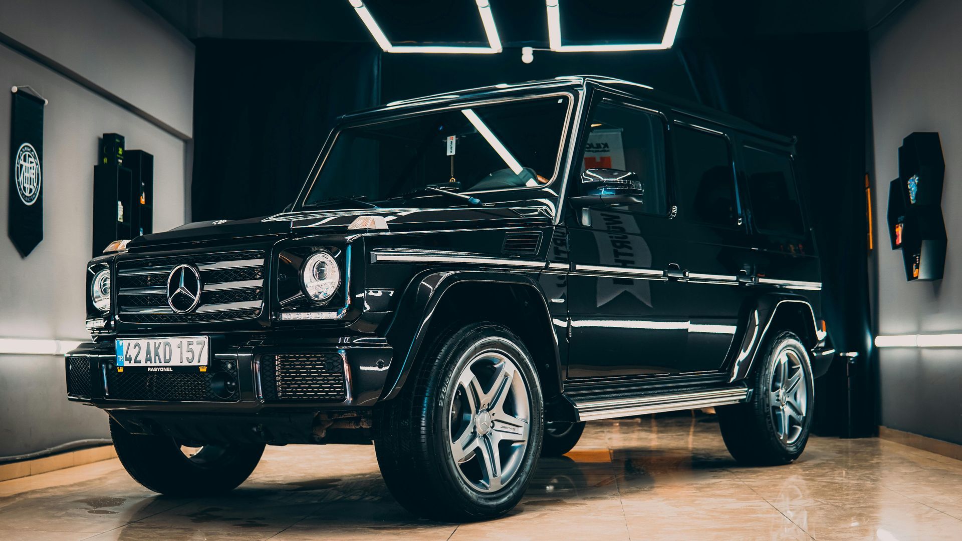 A sleek black Mercedes-Benz G-Class SUV displayed in a modern showroom with dramatic lighting.