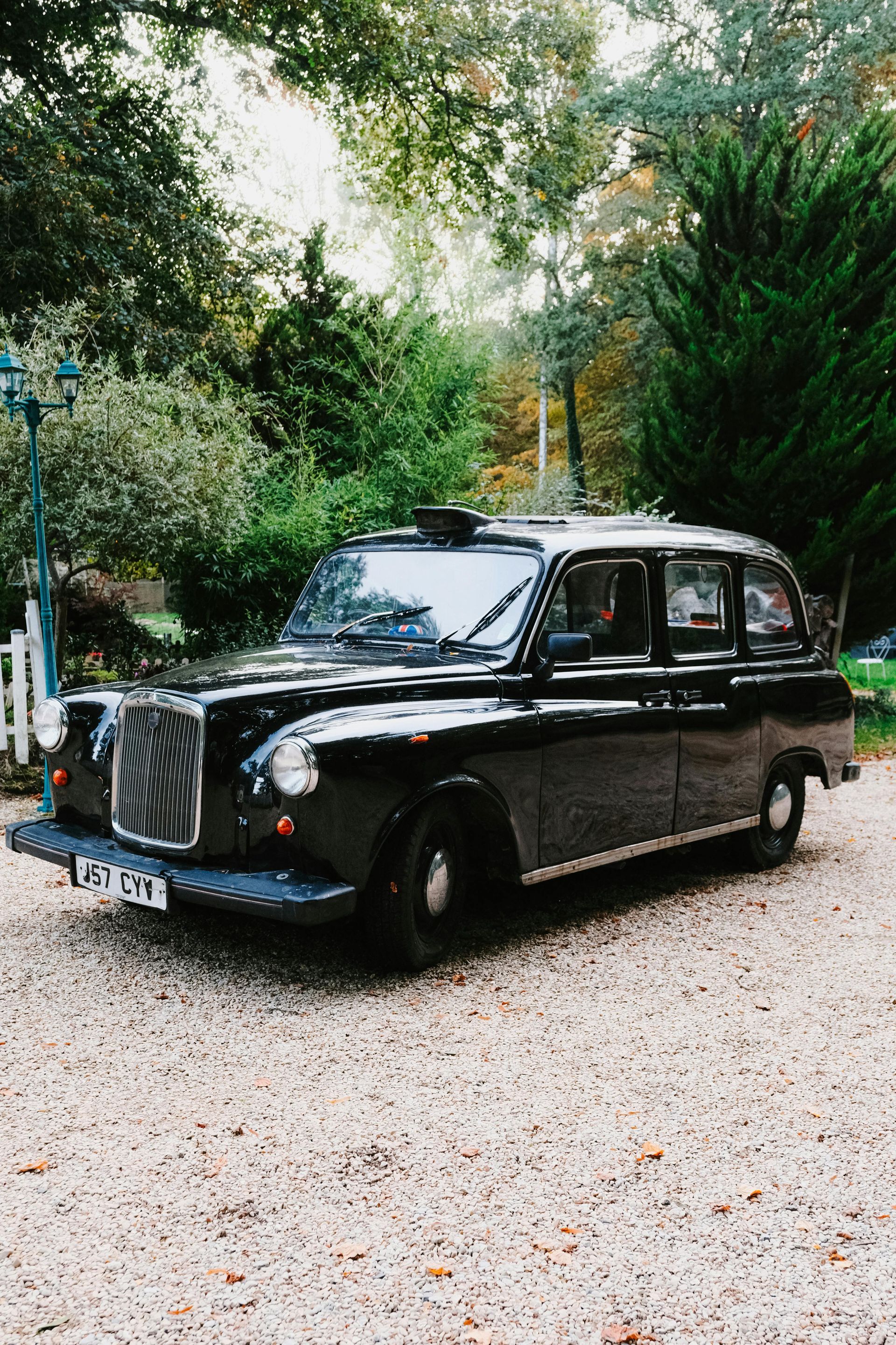 A classic black taxi cab parked on a gravel driveway surrounded by greenery and trees