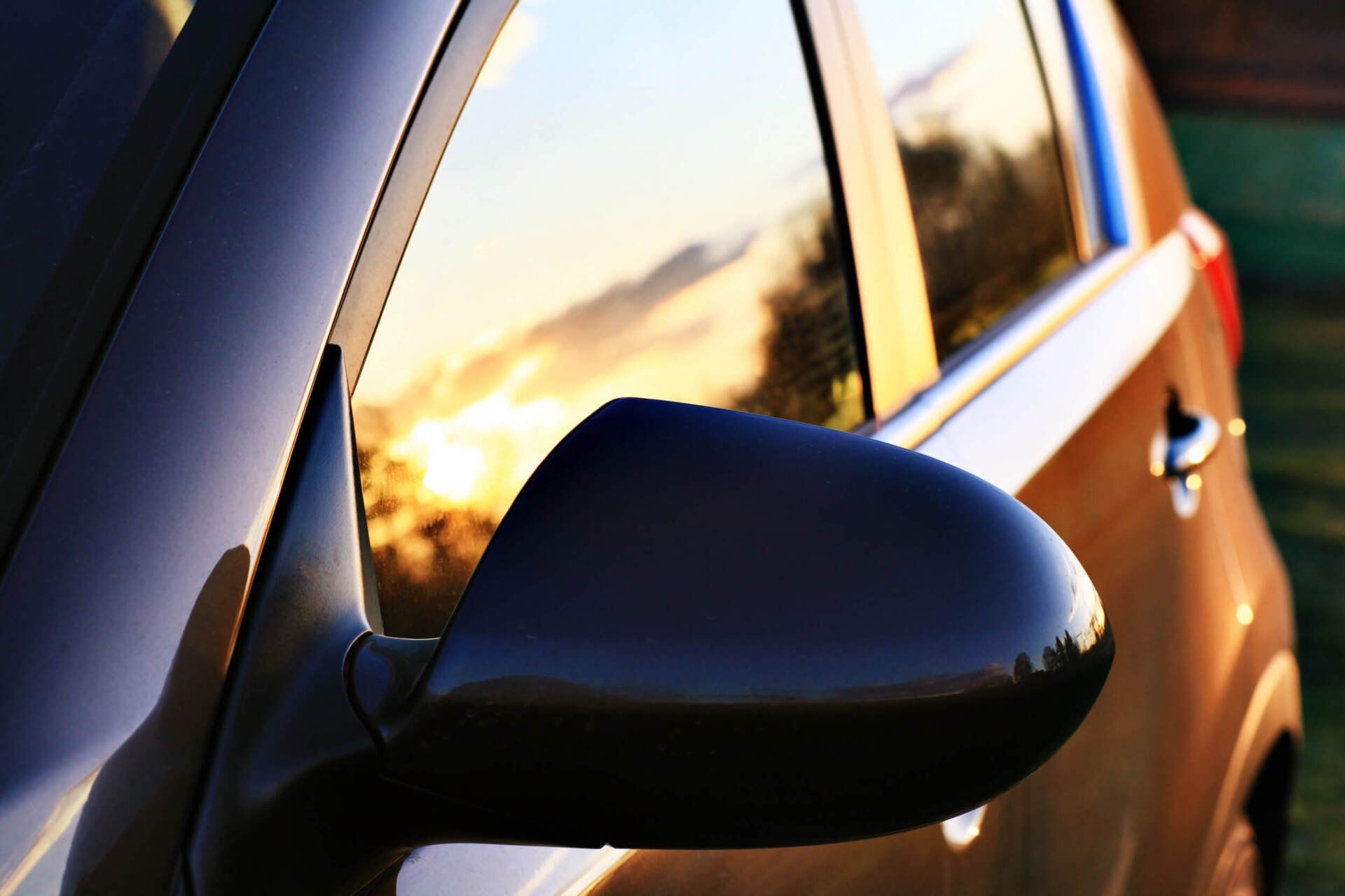 Car's side mirror reflecting a sunset, with car body visible.