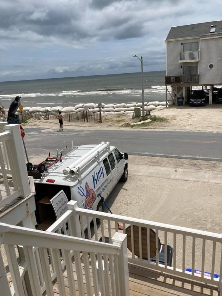 A white van is parked on the side of the road next to a beach.