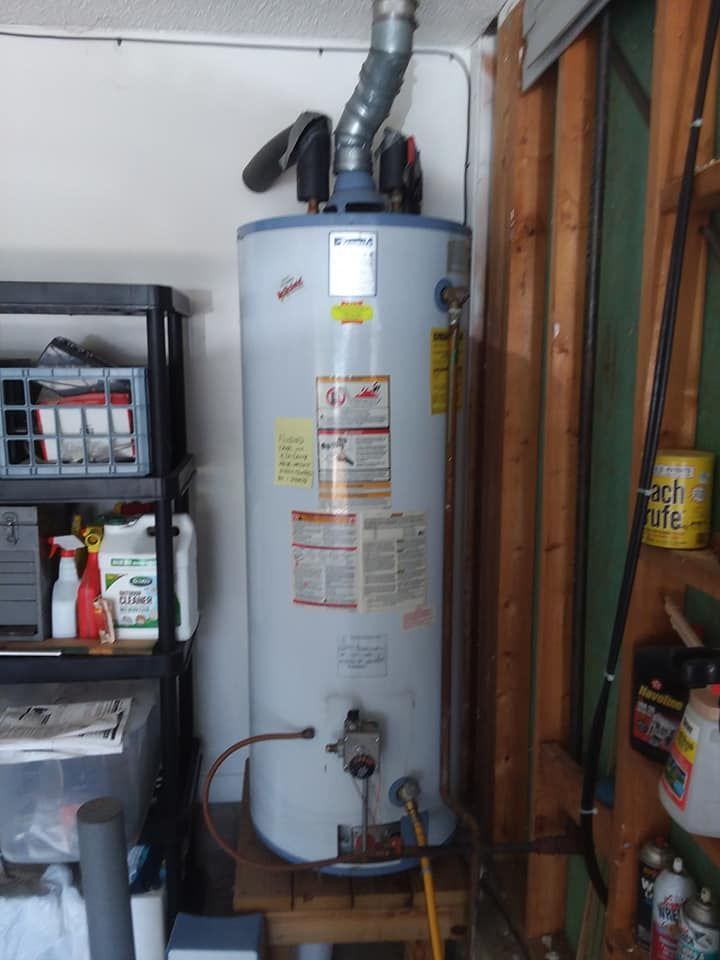 A white water heater is sitting on a wooden shelf in a garage.