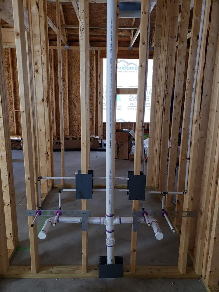 A bathroom in a house under construction with pipes coming out of the wall.