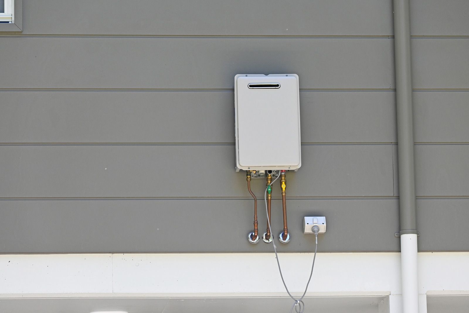A white water heater is attached to the side of a house.
