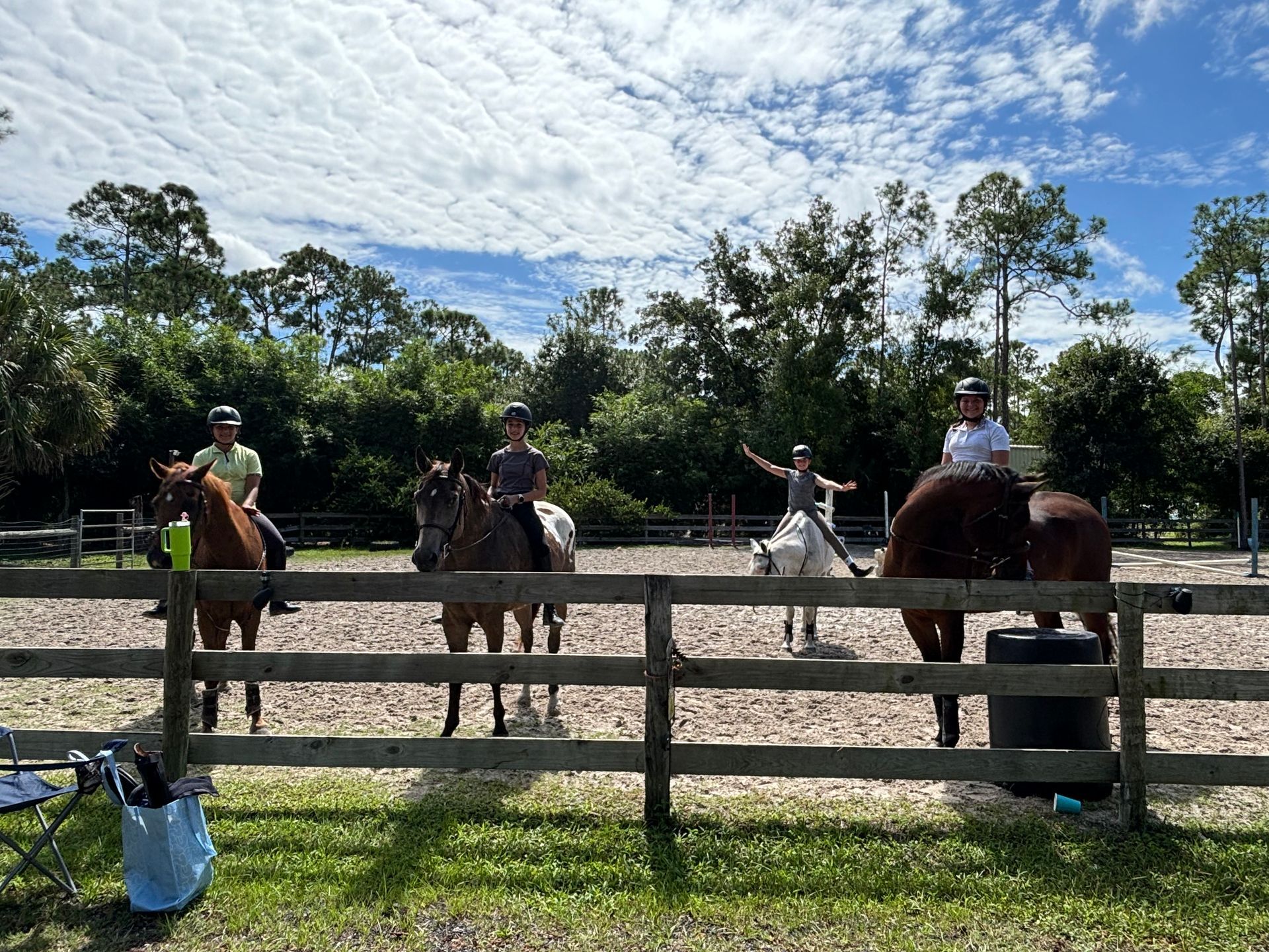 Child riding a small pony in a sandy area. An adult watches nearby, with a dog in the foreground.