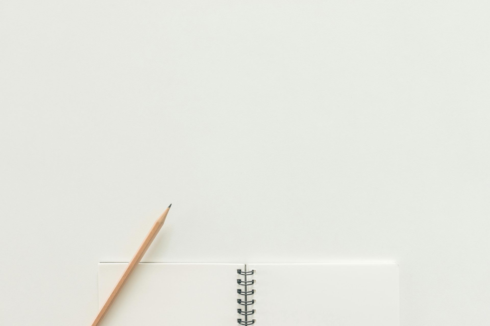 A pencil is sitting on top of a spiral notebook on a white table.