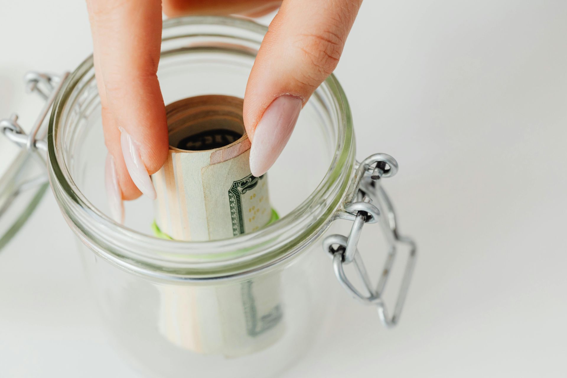 Hand placing rolled-up bills into a clear glass jar.