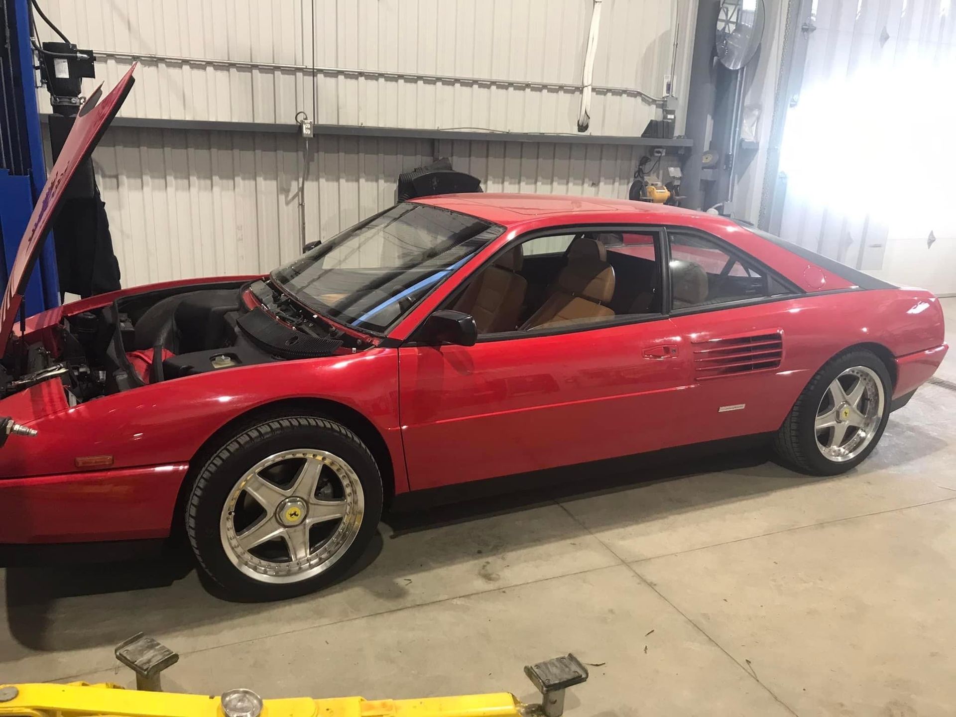 A red car with the hood up is parked in a garage.