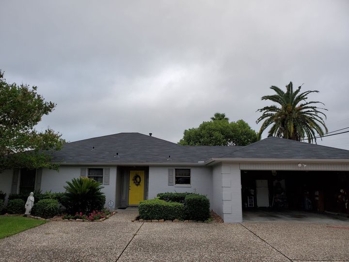 Person on ladder, working on house exterior with power tool.