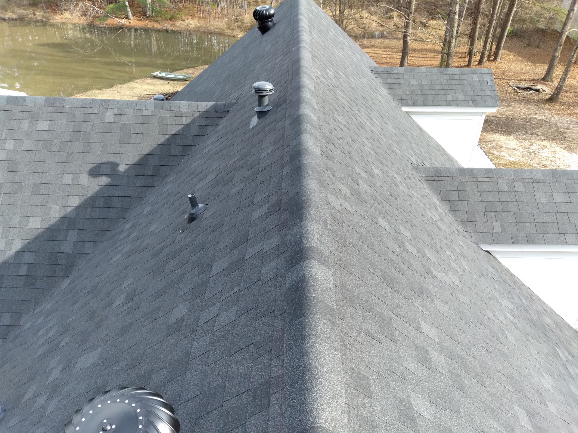 Brown and tan asphalt shingle roof with two vents, green trees, and blue sky.