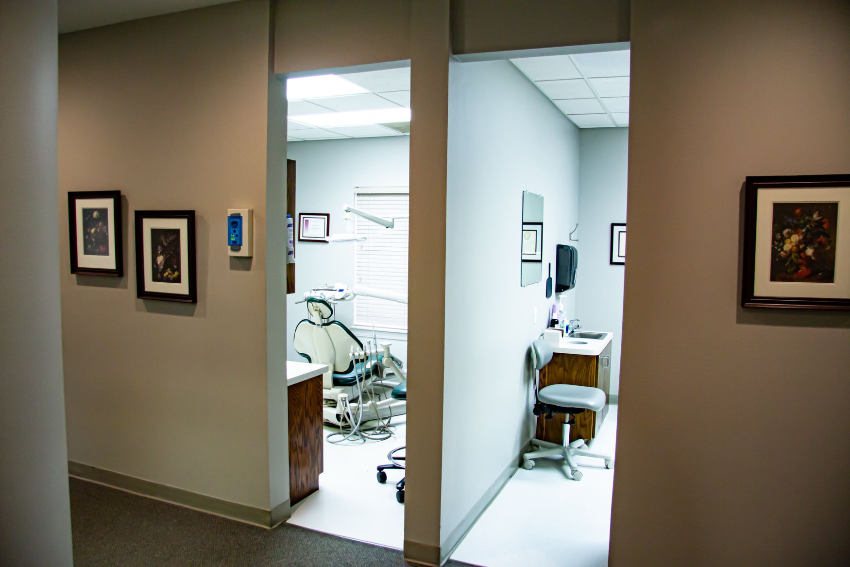 A hallway leading to a dental office with a dental chair and a desk.