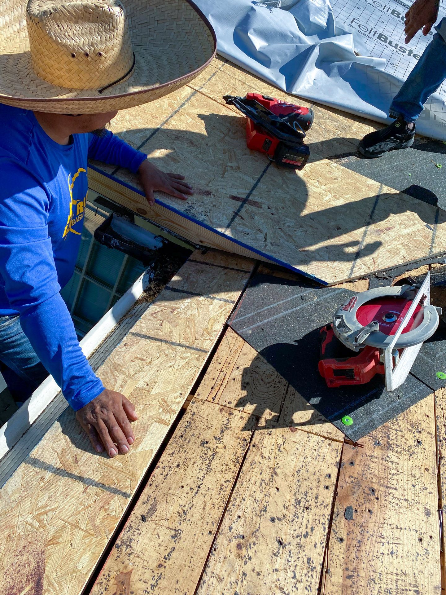 Person on roof installing plywood, using power tools. Sunlight.