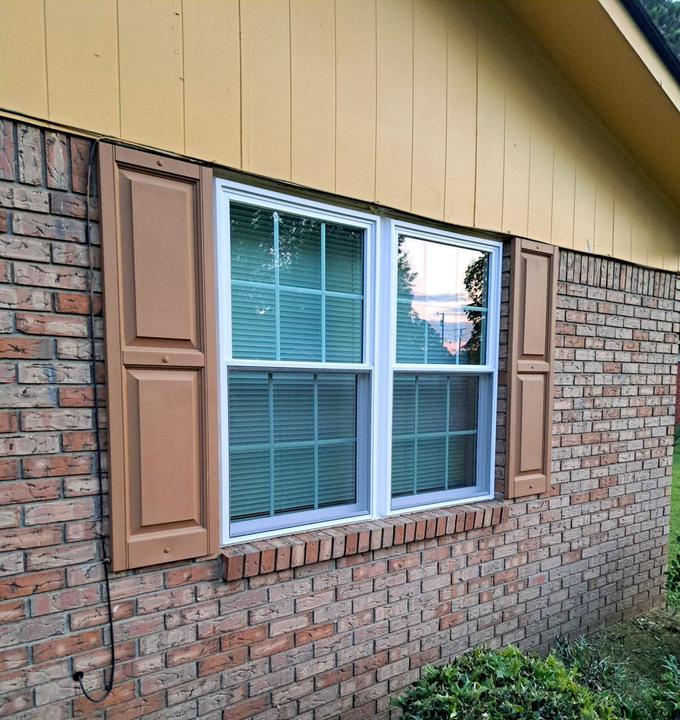 Window with brown shutters on a brick wall, beneath yellow siding.