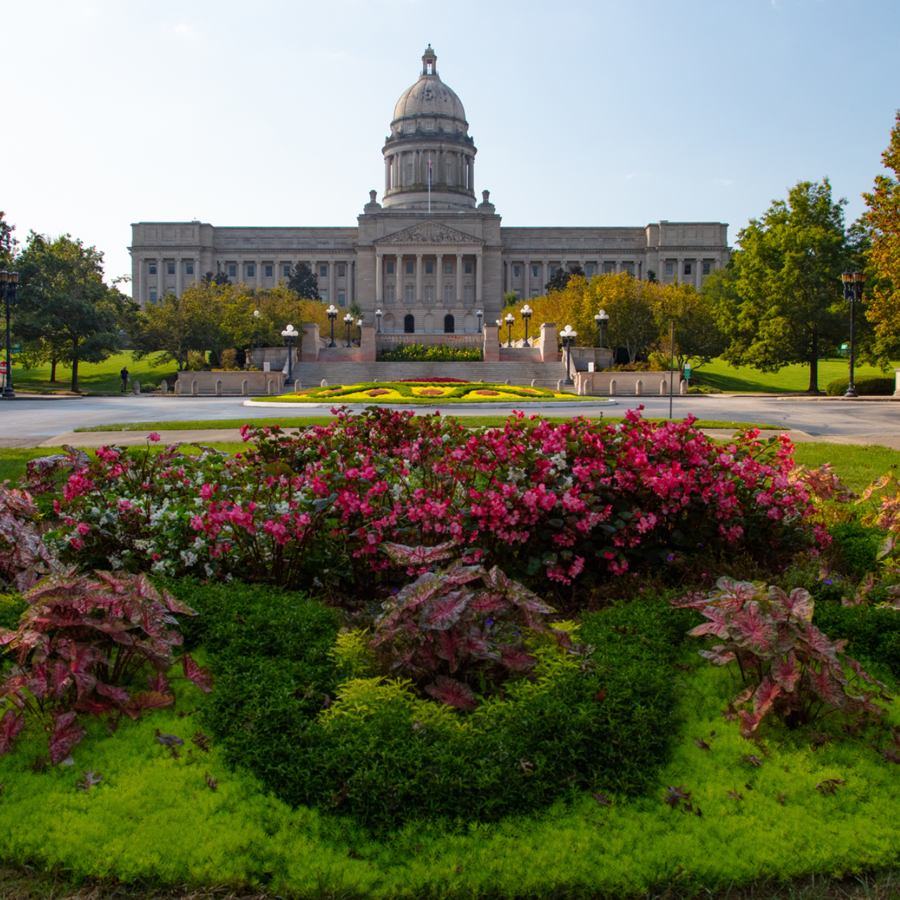 State capitol building behind a colorful flower garden and green lawn under a clear blue sky
