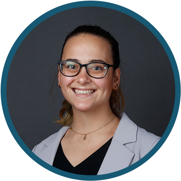 Smiling person with glasses in a light blazer against a dark studio background.