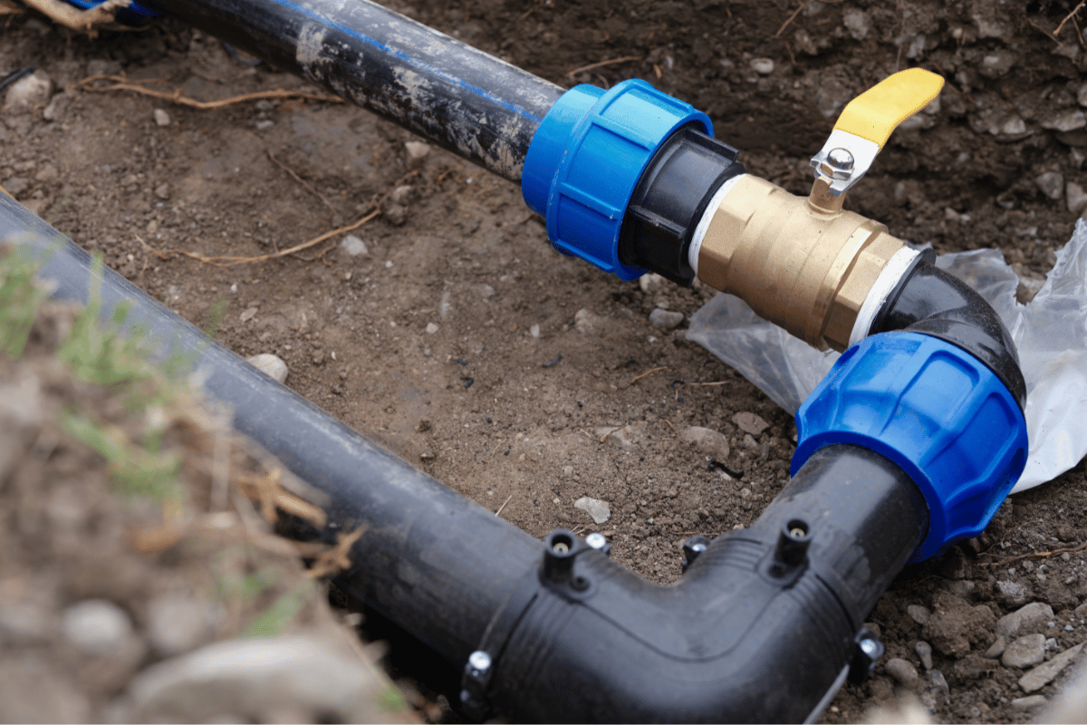 Black water pipes and blue connectors in a trench, with a brass valve.