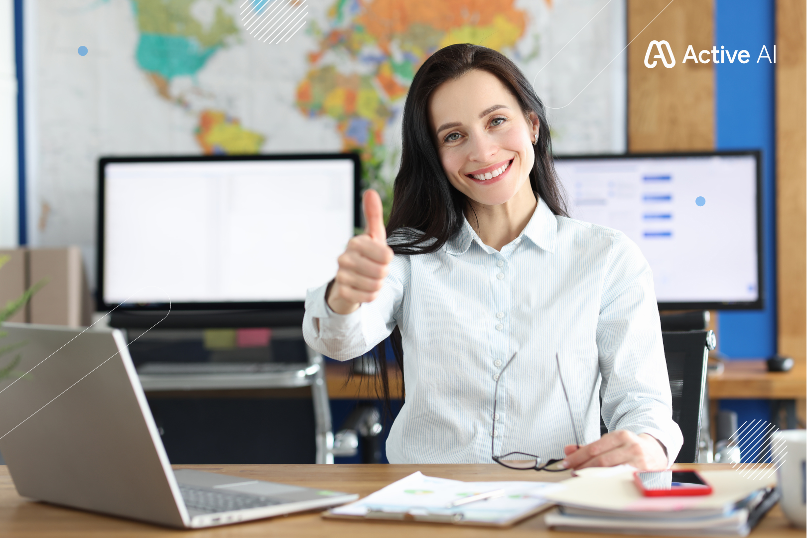 Woman in a white shirt smiling, giving a thumbs up, sitting at a desk with a laptop and papers in an office.
