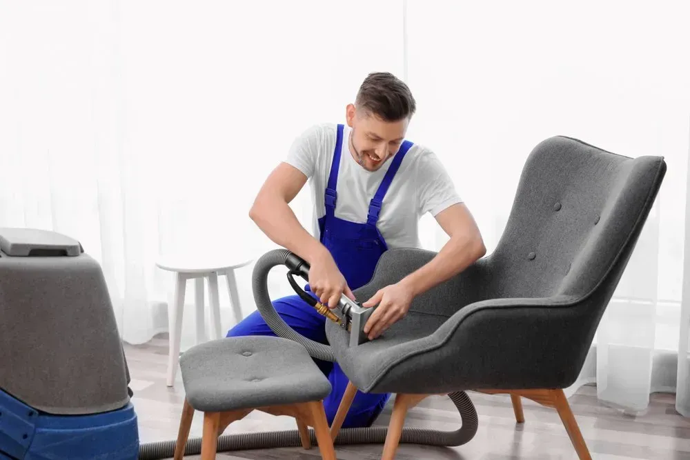 Man Cleaning Gray Armchair With Upholstery Cleaner — Phil Lindfield's Big Red Carpet Cleaning In Taree, NSW