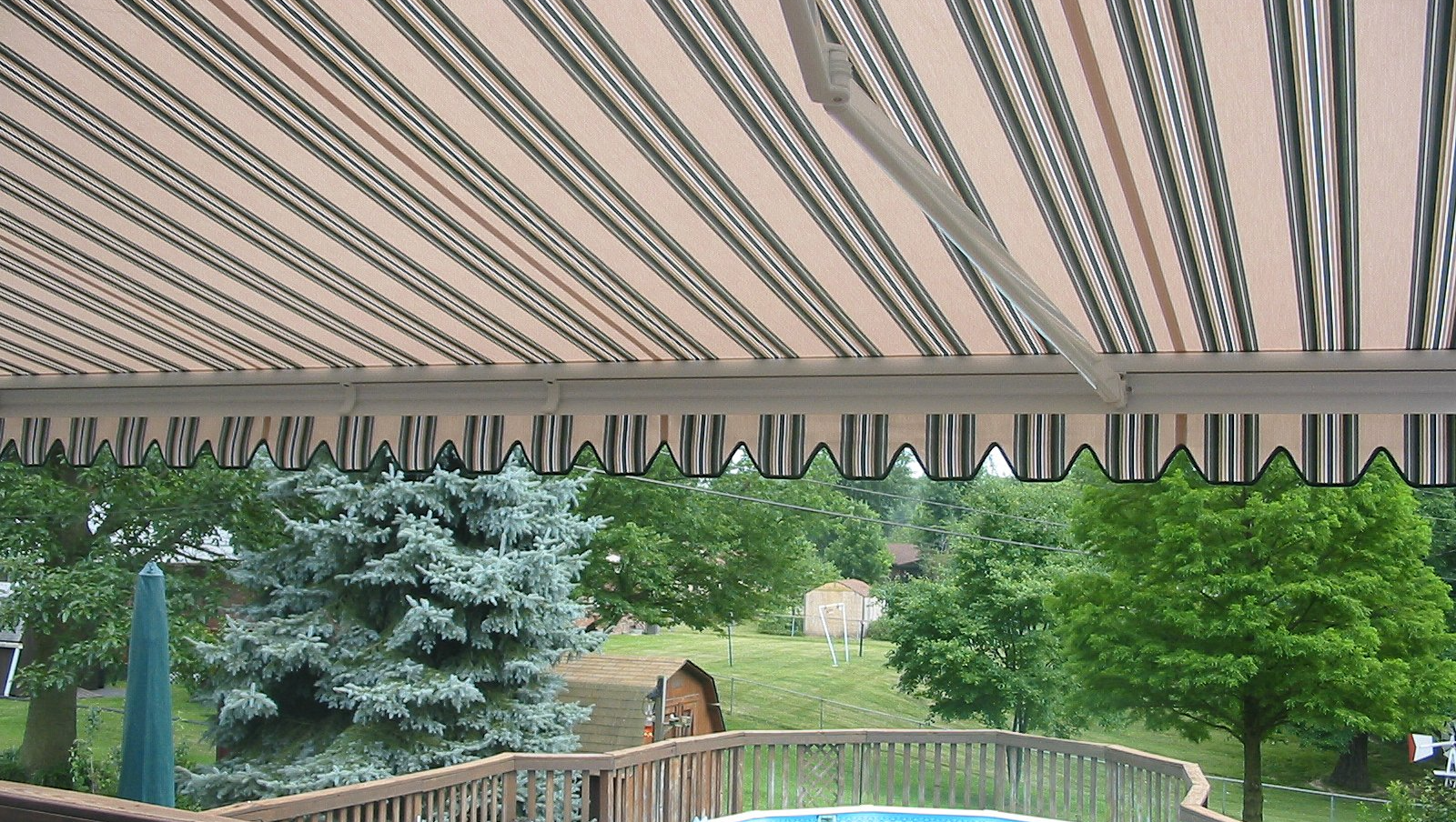 A striped awning over a swimming pool with trees in the background