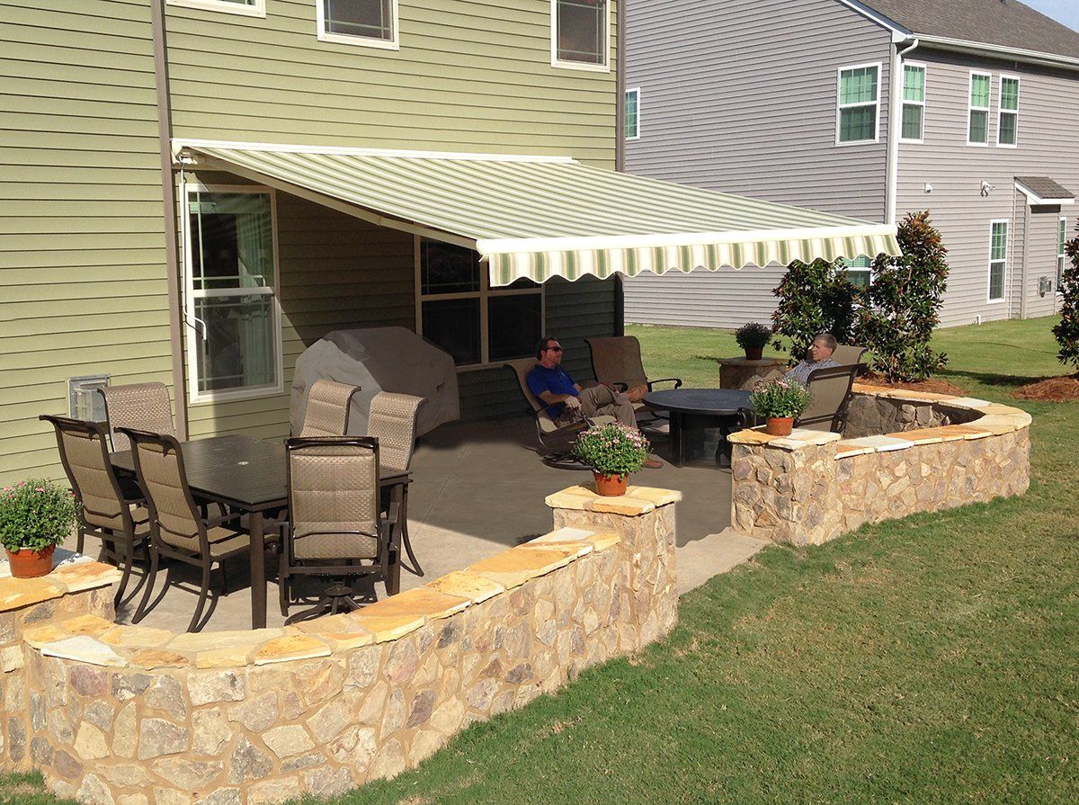 A man sits under an awning on a patio in front of a house