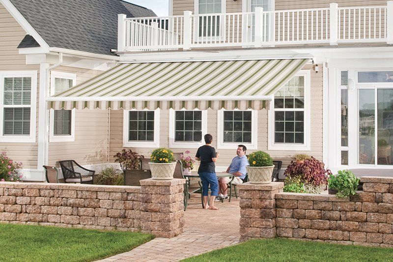 Two men are sitting at a table under an awning in front of a house