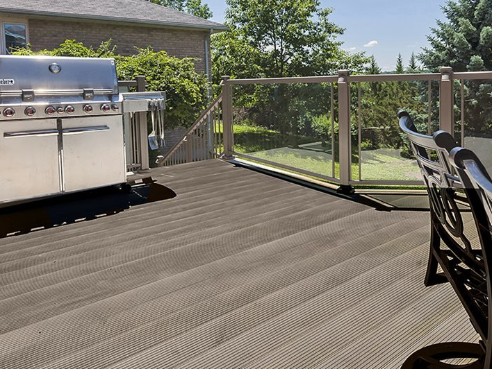 A stainless steel grill sits on a deck next to a bench