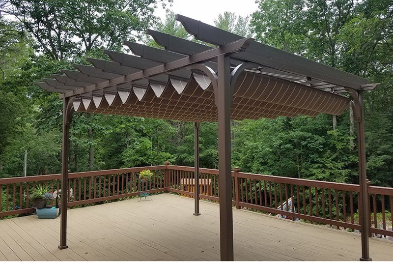 A pergola on a deck with trees in the background