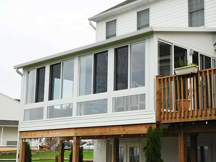 A white house with a large sunroom and a wooden deck.