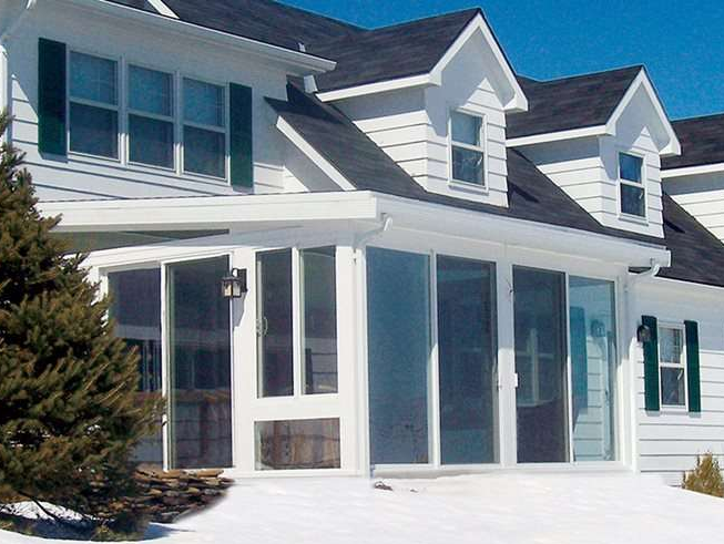 A white house with green shutters is covered in snow