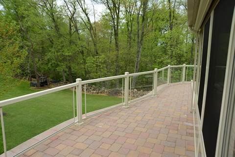 A deck with a glass railing and a brick walkway leading to a lush green field.