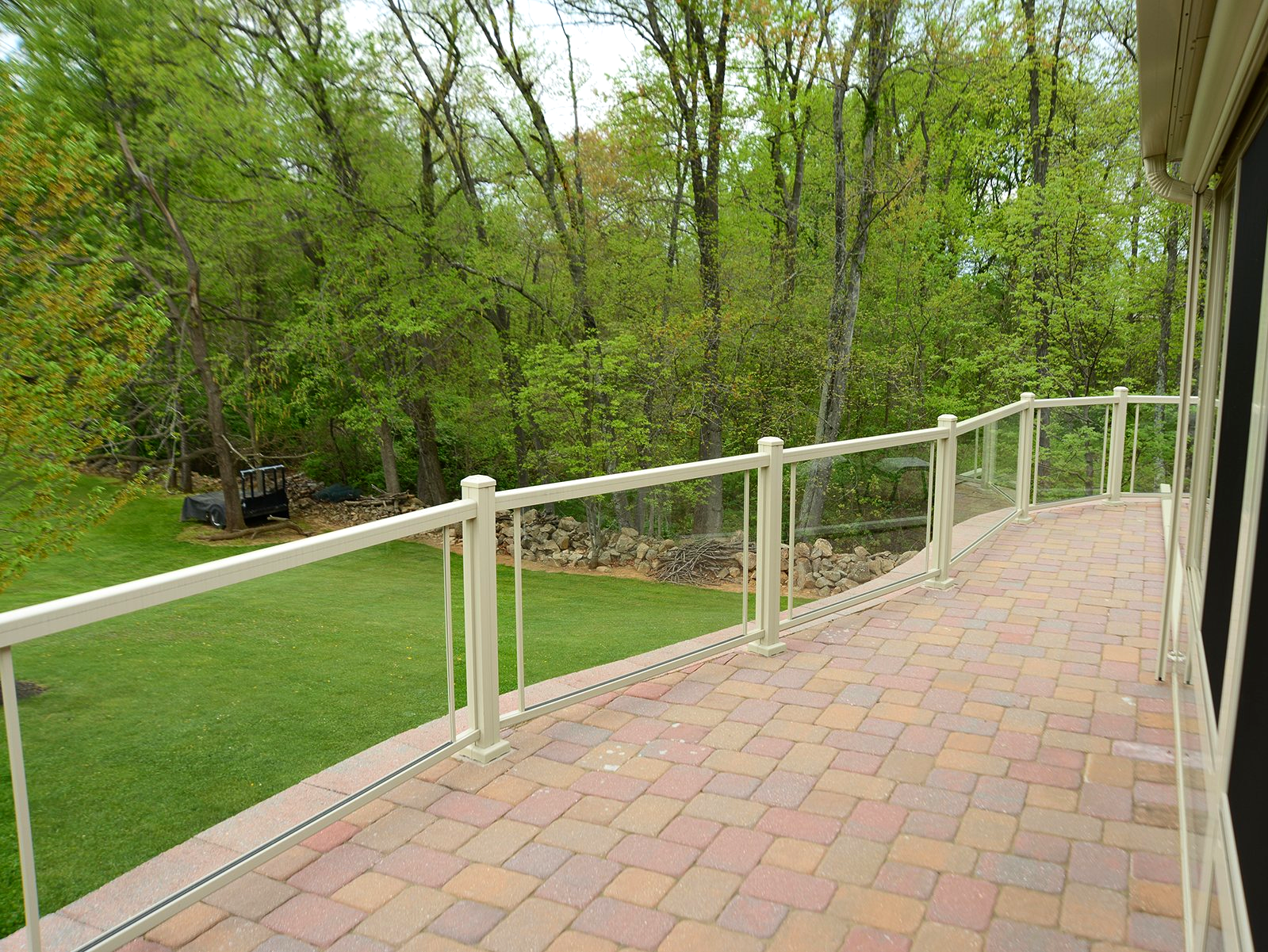 A brick deck with a glass railing and trees in the background