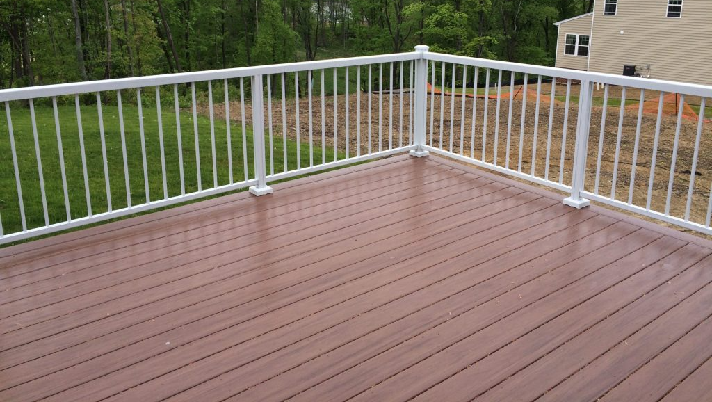 A wooden deck with a white railing and a house in the background