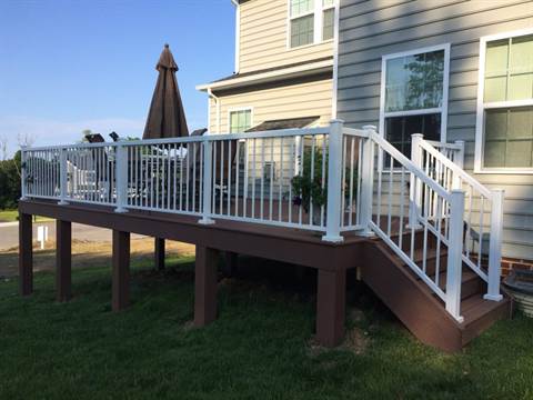 A deck with a white railing and stairs is in front of a house.