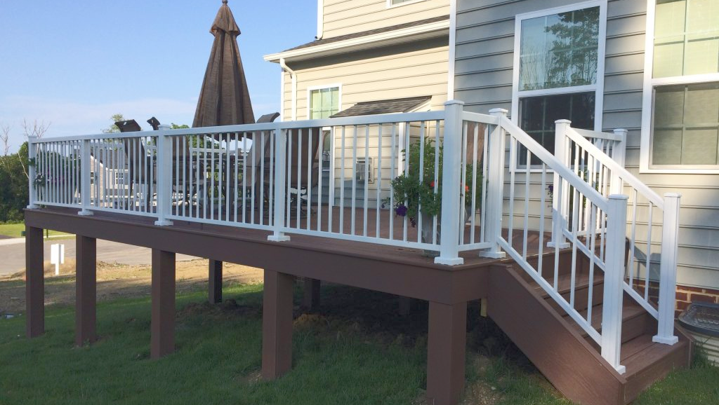 A deck with stairs and a white railing in front of a house